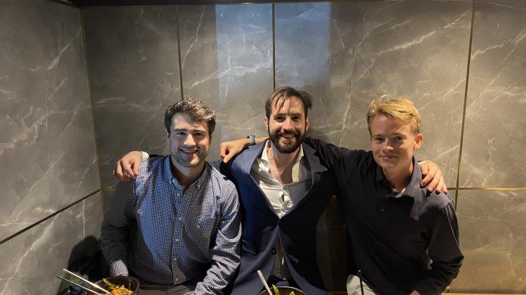 Three men sitting in a restaurant with their arms around each other's shoulders