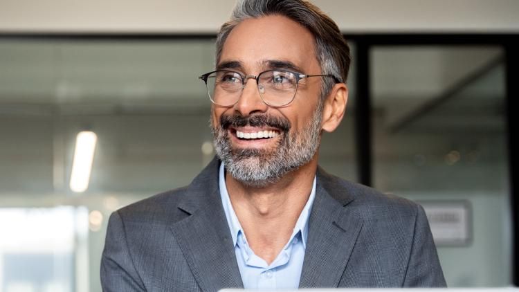 A man wearing glasses sitting in front of his laptop, smiling