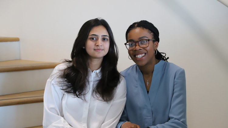 The founders of Dotplot, Shefali Bohra and Debra Babalola, sitting on a flight of stairs together.