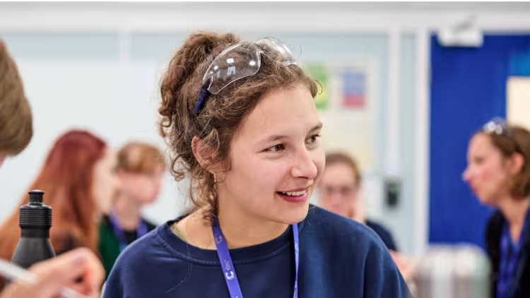 A scientist wearing a blue top in conversation with colleagues. The scientist has curly hair worn in a bun.