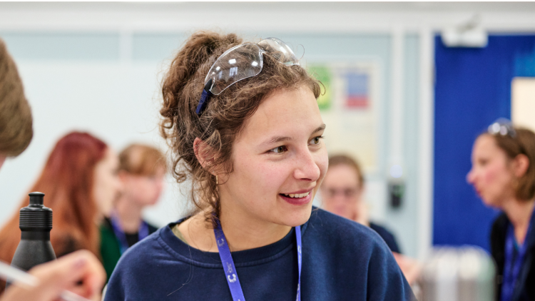 A scientist wearing a blue top in conversation with colleagues. The scientist has curly hair worn in a bun.