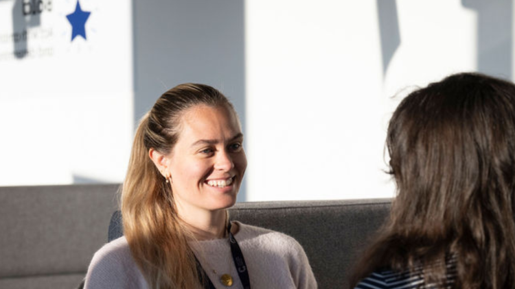 Two women speaking to each other, one with back faced to camera and the other facing camera