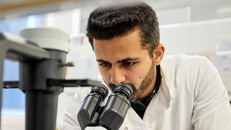 A scientist wearing a lab coat looks through a microscope.
