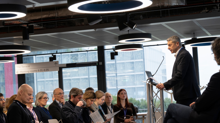 A person in a dark suit standing at a podium, giving a presentation to an audience