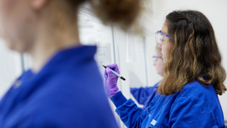 Group of scientists in blue lab coats looking at a white board.