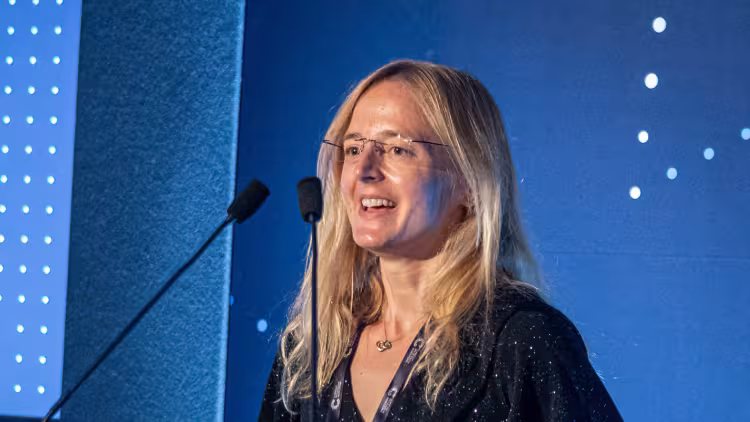 A person with long, blonde hair and a black evening gown giving an acceptance speech at the Awards ceremony.
