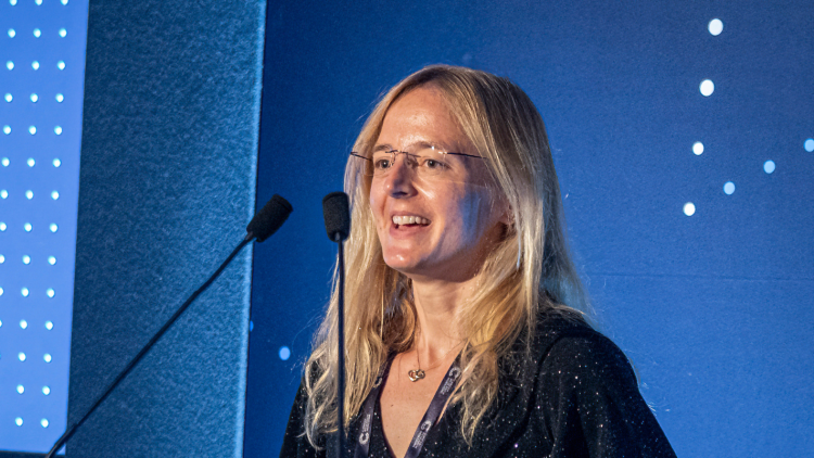 A person with long, blonde hair and a black evening gown giving an acceptance speech at the Awards ceremony.