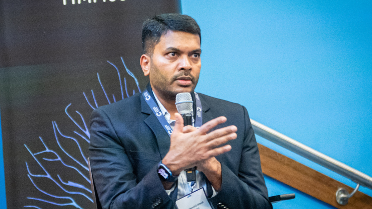 A speaker at the Innovation Summit holding a microphone. They wear a dark blazer and white shirt. 