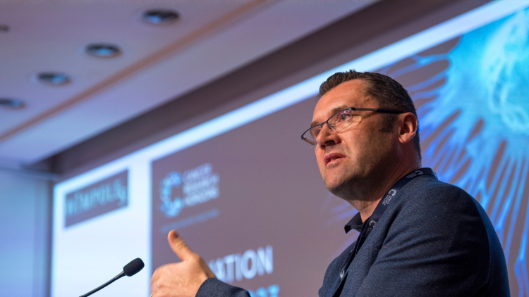 A person wearing glasses, short dark hair and a dark blazer giving a talk at the Innovation Summit