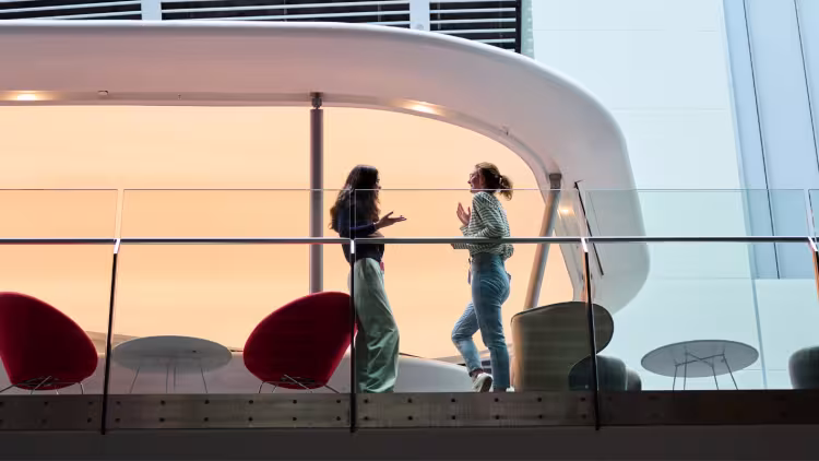 Two woman speak to each other on an inside balcony, with the photo taken from the floor