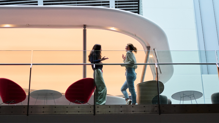 Two woman speak to each other on an inside balcony, with the photo taken from the floor