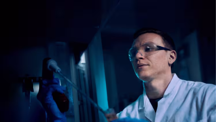 A scientist wearing google and a lab coat examining a sample.