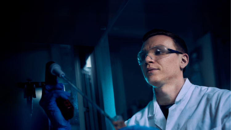 A scientist wearing google and a lab coat examining a sample.
