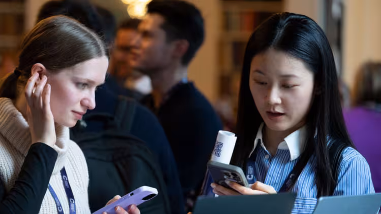 Two people connect at a networking event. One of them wears a white and black top, while the other wears a blue blouse. 