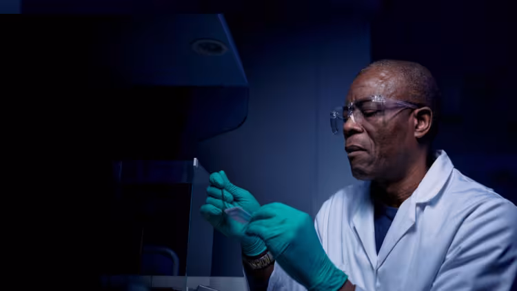 Scientist wearing a white lab coat and goggle looking at some equipment.