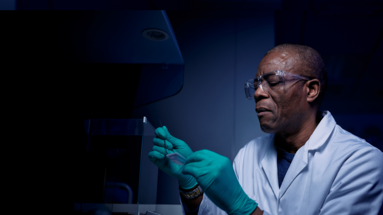 Scientist wearing a white lab coat and goggle looking at some equipment.