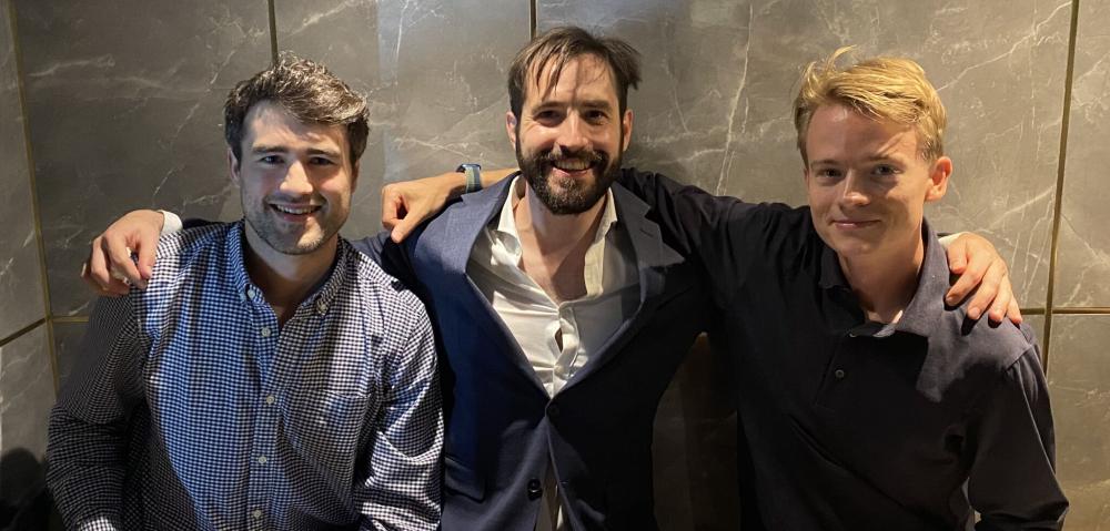 Three men sitting in a restaurant with their arms around each other's shoulders