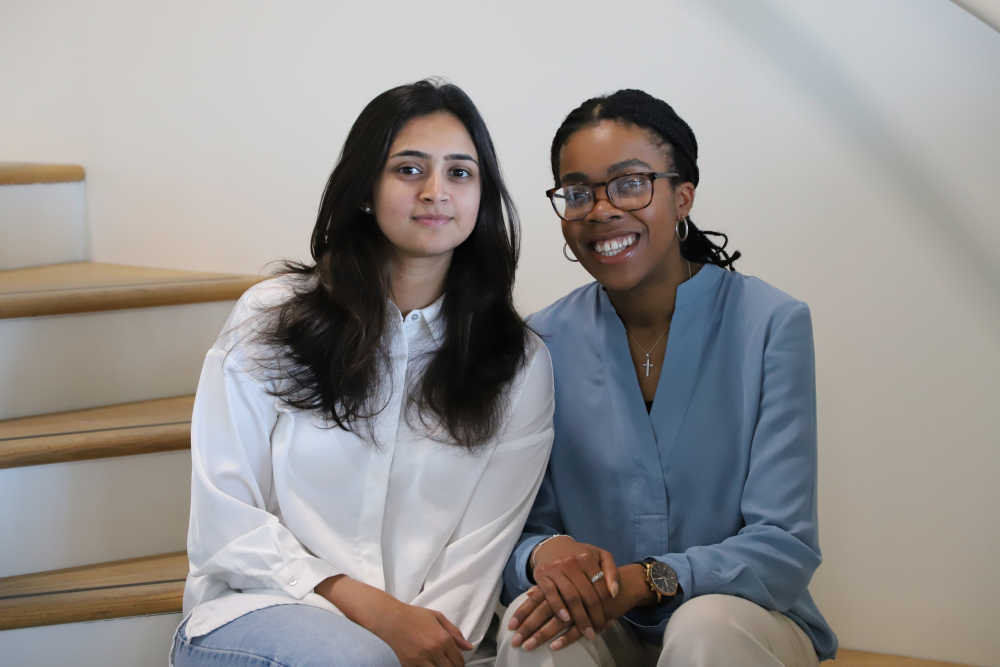 The founders of Dotplot, Shefali Bohra and Debra Babalola, sitting on a flight of stairs together.