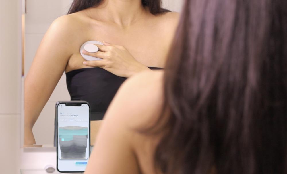 A woman using the Dotplot device and app to perform a breast self-check.