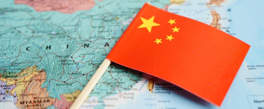 A photo of the China section of a world map with a small Chinese flag laying on top